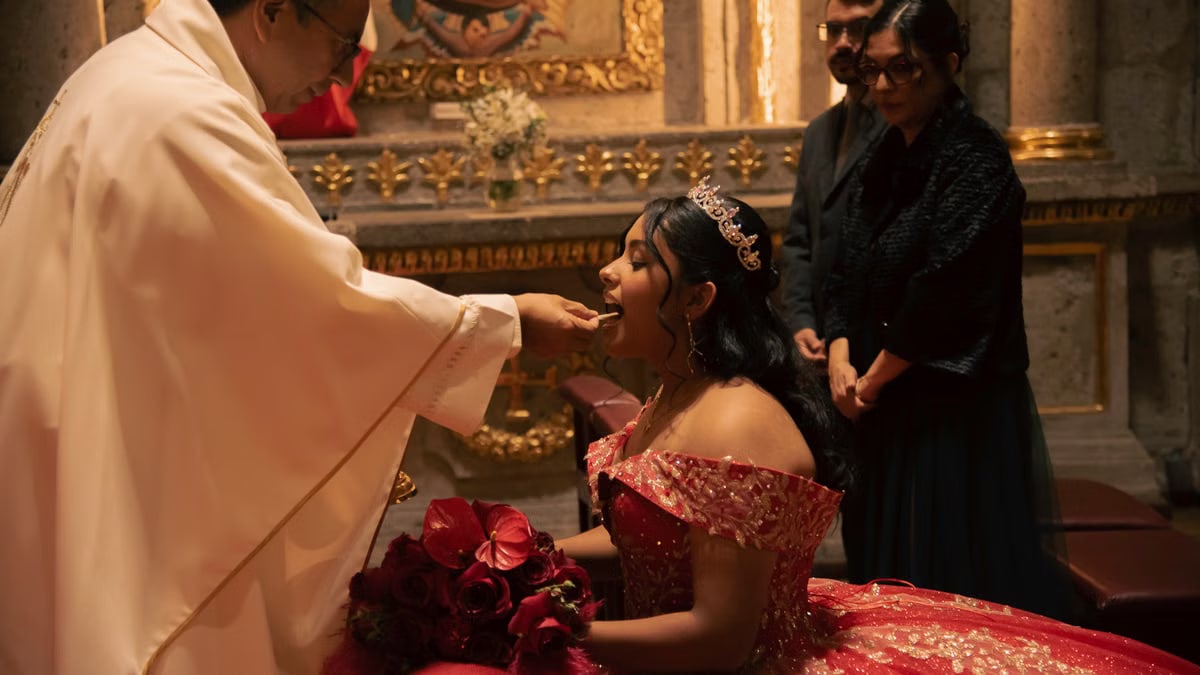 Young woman in red gown receives communion during her quinceañera in a beautifully decorated church.