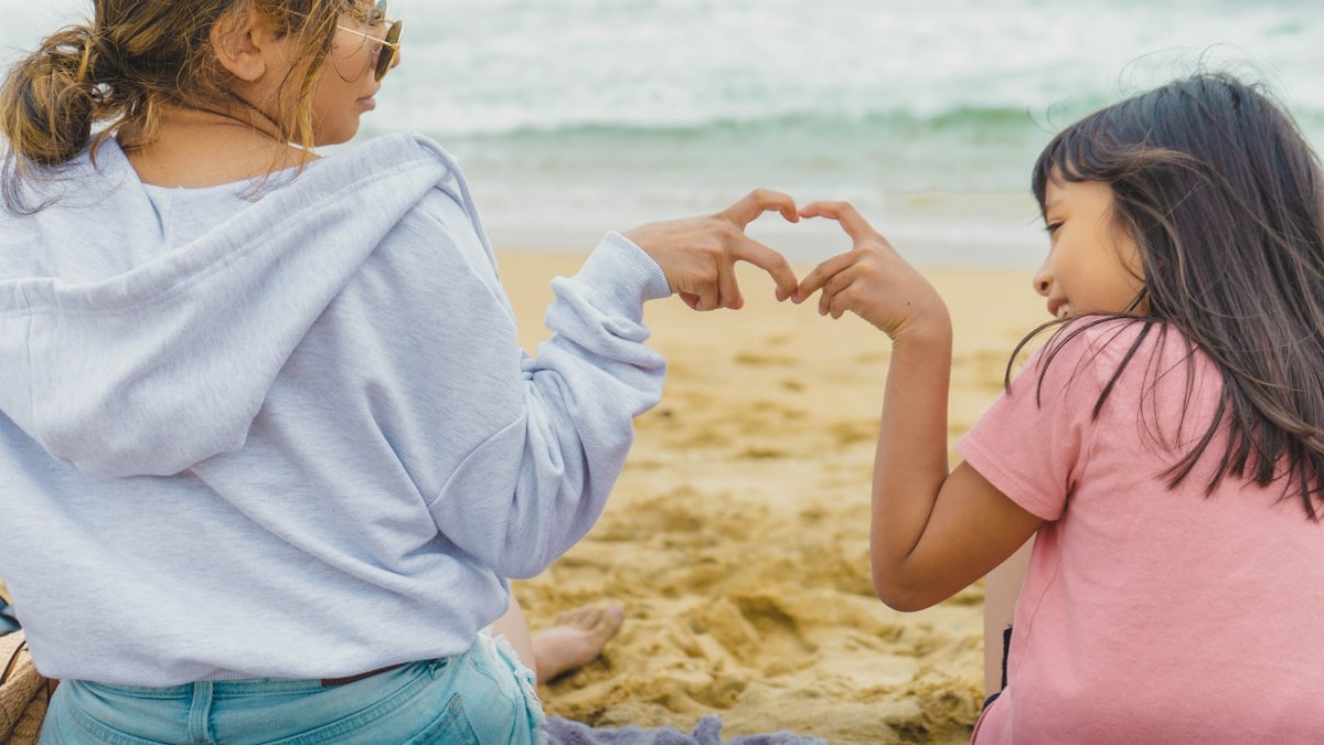 girl in white long sleeve shirt and blue denim shorts sitting on beach shore during daytime